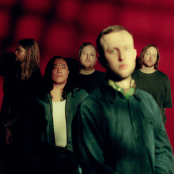 Artist La Dispute standing in front of red wall with black pattern on left